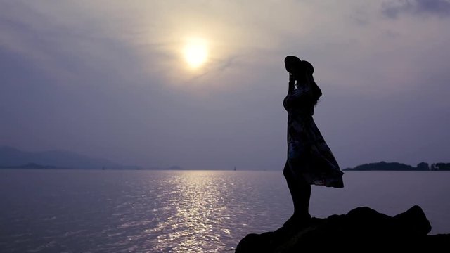 A lonely girl stands on the stones on the beach, admires the evening and the sunset. slow motion, 1920x1080, full hd