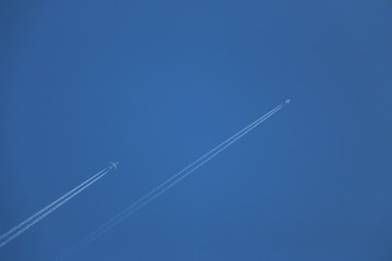two jet planes fly in a clear blue sky, leaving a white trail. two aircraft leave condensation traces in a clear blue sky