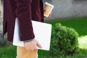 cropped shot of man holding laptop and coffee to go on street