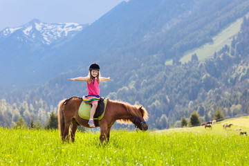 Kids riding pony. Child on horse in Alps mountains