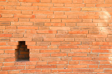 Brick wall with a hole in public garden in sunny day.