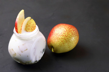 Food. Dessert of milk. Dairy product on a black background. Creamy yogurt in a glass jar with pieces of fresh juicy pears for a healthy diet.