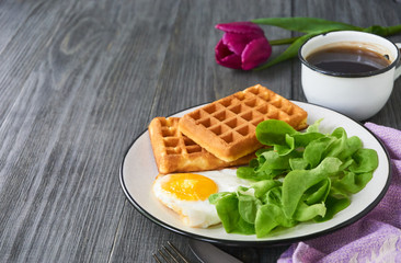 Breakfast with fried egg, fresh lettuce and waffles