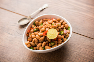 Boiled Peanut Chaat or Chatpata sing dana or shengdana or mungfali. served in a ceramic bowl over moody background