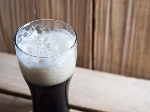 A glass of cold dark beer on a wooden table