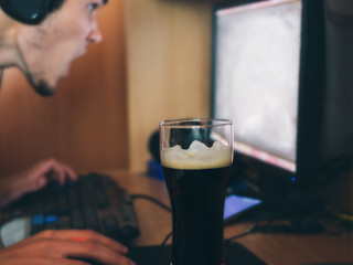 The guy drinks beer and plays at the computer