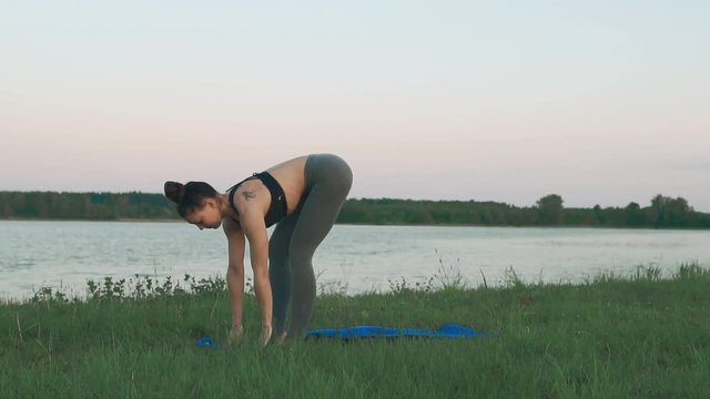 Young woman wearing doing yoga in morning at lake on blue yoga mat in quiet scenery. Woman doing yoga. Healthy lifestyle concept in slow motion with copyspace