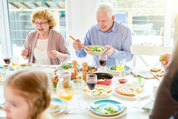 Obraz na płótnie Canvas Portrait of happy family enjoying dinner together sitting round festive table with delicious dishes, focus two grandparents, copy space