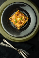 Traditional Lasagna With Minced Beef, Bolognese Sauce and Basil on Dark Plate. Italian Cuisine.