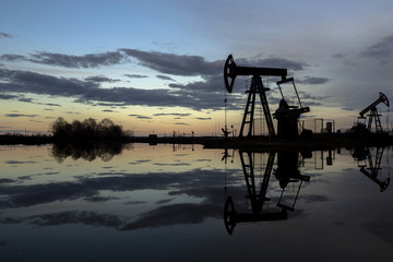 Naklejka premium The beam pumping unit is homework, sunset in oil field. Oil pump oil rig energy industrial machine for petroleum. The pumping unit as the pump installed on a well. Equipment of oil fields.