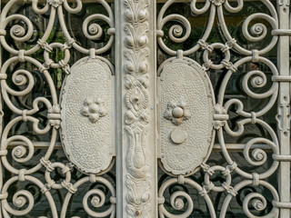 White magnificent wrought-iron gates, ornamental forging, forged elements close-up.