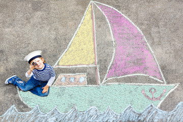 Little kid boy having fun with ship picture drawing with chalk
