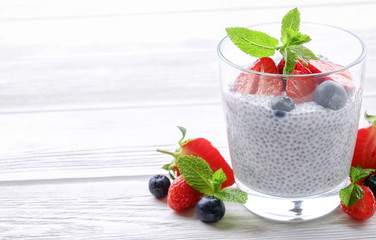 Portion of chia pudding with vegan almond milk, blueberry & strawberry, mint, served in glass. Healthy vegetarian breakfast, seeds, berries, greek yogurt, wooden table. Background, close up, top view.