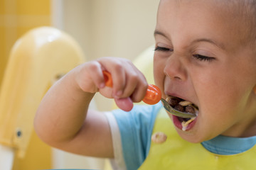 The boy 2 years eats porridge. Children's table. The concept of the child's independence. funny kid in a baby seat.