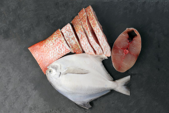 White pomfret Spanish mackerel red snapper fish cleaned descaled degutted sliced fillet pieces on black marble slate background