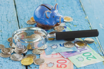 Canadian dollars, piggy bank, coins and a magnifying glass on the wooden background