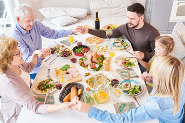High angle portrait of big happy family joining hands in prayer at dinner holding hands during...