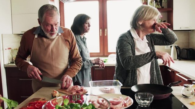Senior couple cooking dinner together with friends at home.