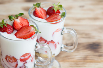 Tasty spring dessert with organic strawberry and cream in glass on a wooden table in rustical style