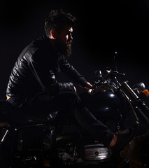 Fototapeta na wymiar Macho, brutal biker in leather jacket riding motorcycle at night time, copy space. Bikers leisure concept. Man with beard, biker in leather jacket sitting on motor bike in darkness, black background.