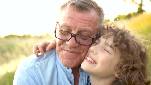 Close-up portrait of a curly schoolboy with his grandfather. The man joyfully hugs his grandson. Happy Family Vacation