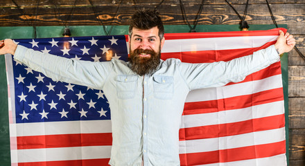 American teacher holds american flag. Man with beard and mustache on happy face holds flag of USA, wooden background. American educational system concept. Student exchange program.