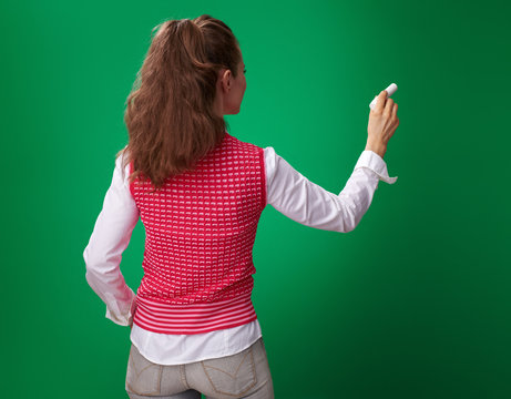 student woman writing with piece of chalk on green background