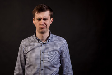 A dark haired white man with a sad and boring face and displeasingly emotion closed eyes in a plaid shirt and jeans on a black isolated background