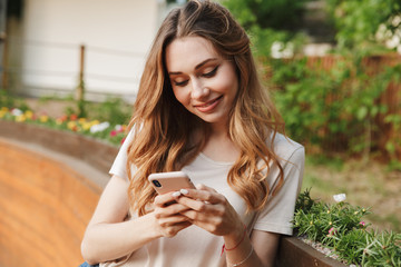Smiling young girl in casual clothes using mobile phone