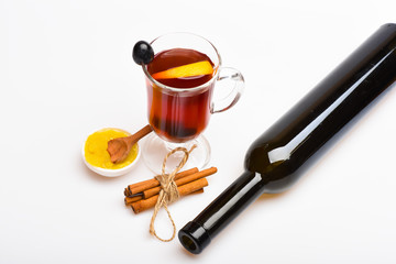 Glass with mulled wine with grape and cinnamon and bottle of wine. Glass with mulled wine or hot drink with grape, cinnamon and honey, white background, close up. Seasonal beverage concept