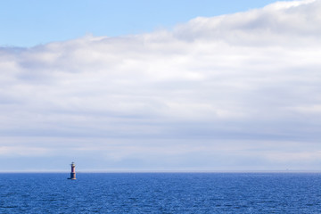 Seascape with navigation mark (buoy or beacon) in the distance. Blue water and cloudy sky background with copy space