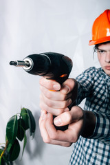 attractive and confident constructor carpenter or builder man working wood with electric drill at industrial construction site.The builder or the repairman holds in his hand a drill