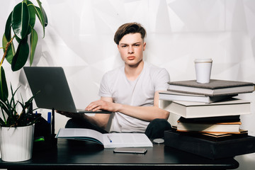 Business concept.Young charming man is focussed looks at laptop while working at table on gray background. works on new startup project, makes internet researches, analyzes data.Place for text or ads