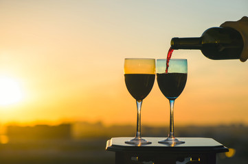 Female hand with bottle pours red wine into glasses on blurred night city background. Service on the roof of the restaurant