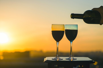 Female hand with bottle pours red wine into glasses on blurred night city background. Service on the roof of the restaurant