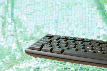 Part of black computer keyboard floating on mint green and white bokeh background. Copy space.