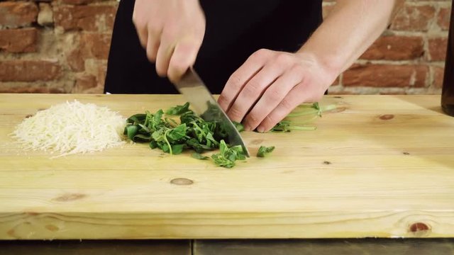 Preparation of pesto sauce. The chef cutting green leaves of basil up on a wood chopping board in the kitchen of a restaurant. 4K