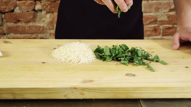 Preparation of pesto sauce. Grated parmesan cheese and fresh chopped basil on wood cutting board. 4K