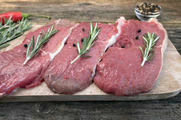 Raw pork steak with black pepper peas and rosemary close-up on a wooden background