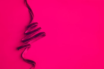 Christmas tree made with dark pink velvet ribbon curles on colored background. Minimalism concept. Copy space for text, horizontal
