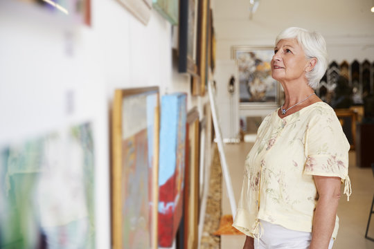 Senior Woman Looking At Paintings In Art Gallery