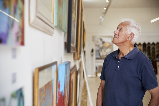 Senior Man Looking At Paintings In Art Gallery