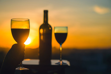 Silhouette female hand toasting wine on sunset background. Romantic couple celebrating at a restaurant