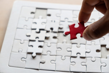 Hand holding piece of blank jigsaw puzzle with paper frame background.
