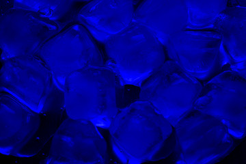 Blue ice cubes with water drops on a reflective surface close-up