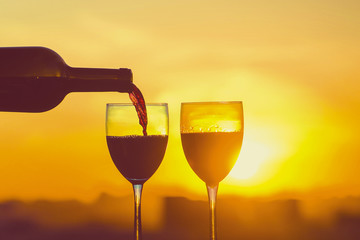 Female hand with bottle pours red wine into glasses on blurred night city background. Service on the roof of the restaurant