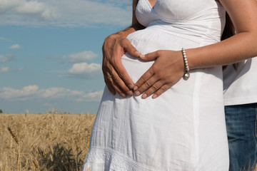 man hugs pregnant woman, heart from hands