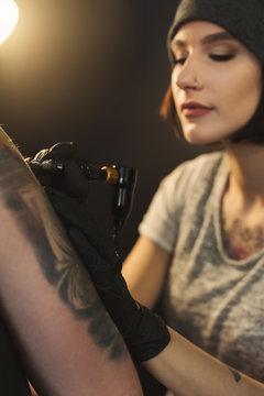 Young woman tattooist doing tattoo on shoulder