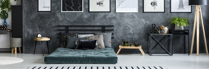 Simple posters hanging on texture wall in dark grey bedroom interior with fresh plant, mattress...