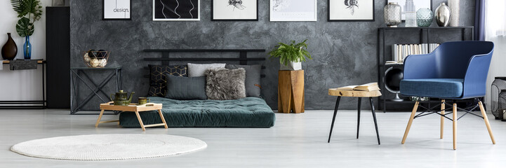 Wooden tray with green jug and tea cup standing next to mattress with pillows in dark grey bedroom interior with texture wall